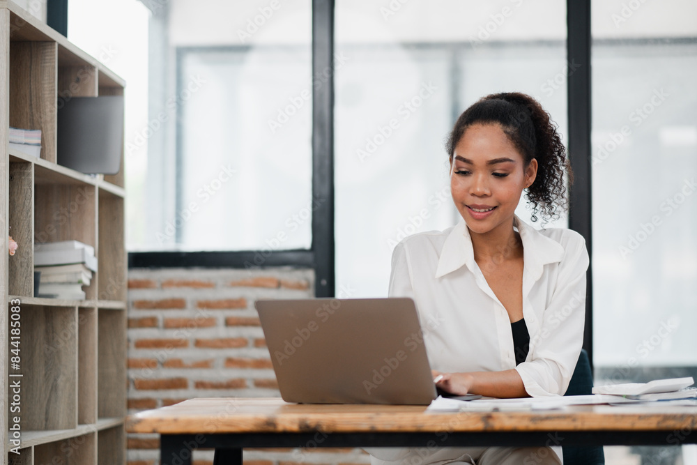Young woman working on a laptop in a modern office with brick wall and large windows, showcasing a productive work environment. Young woman working on a laptop in a modern office with brick wall and large windows, showcasing a productive work environment.