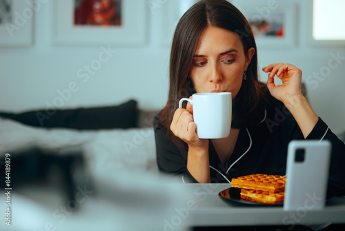 Woman Having Breakfast in Bed Watching the News on her Phone. Lady checking social media while drinking her morning coffee 
 photo