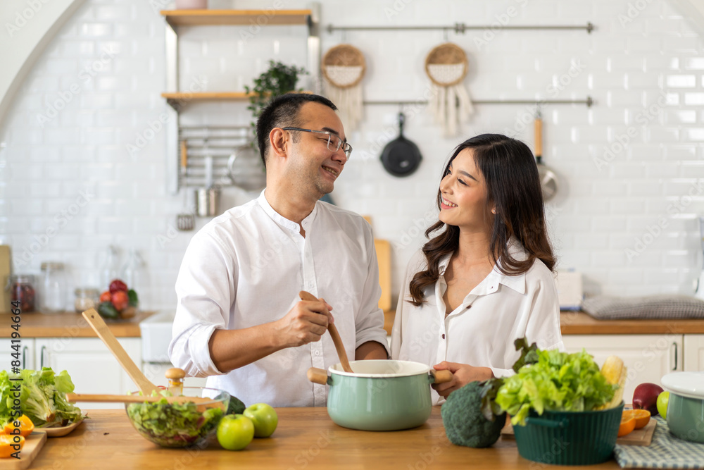 Asian happy couple cooking together with fresh and healthy meal in modern kitchen, stirring a pot while the woman with fresh vegetables and ingredients healthy and lifestyle, love and teamwork at home Asian happy couple cooking together with fresh and healthy meal in modern kitchen, stirring a pot while the woman with fresh vegetables and ingredients healthy and lifestyle, love and teamwork at home