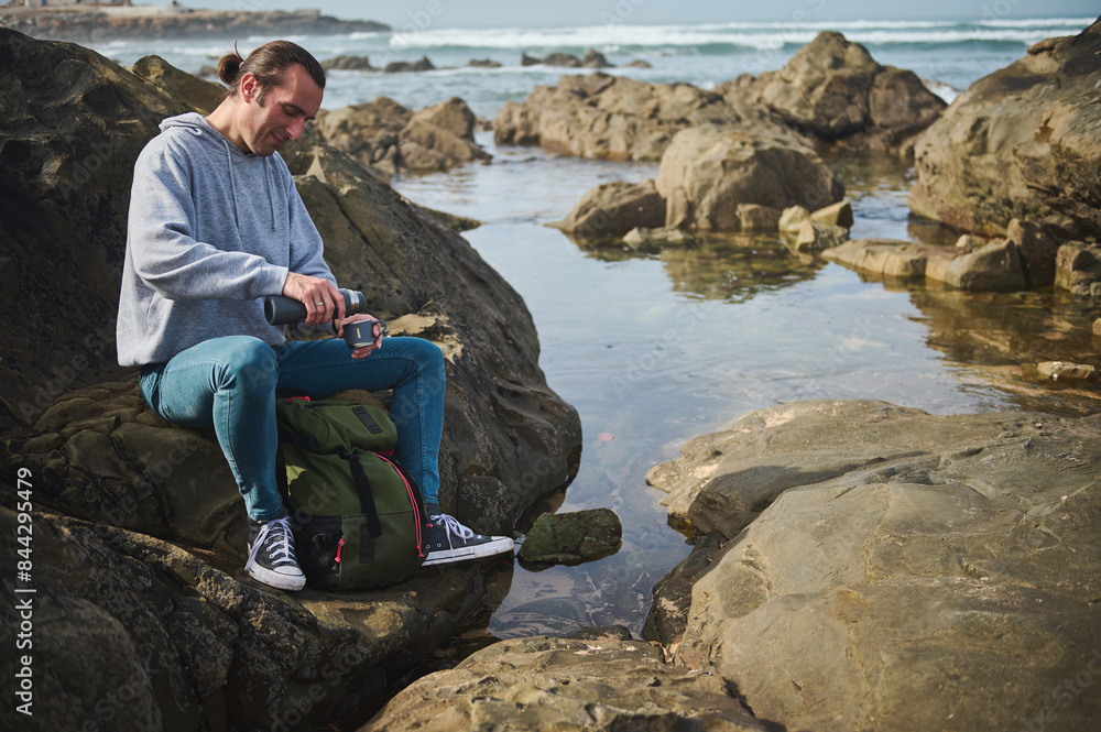 Man enjoying a peaceful moment by the rocky sea shore while preparing a hot beverage Man enjoying a peaceful moment by the rocky sea shore while preparing a hot beverage