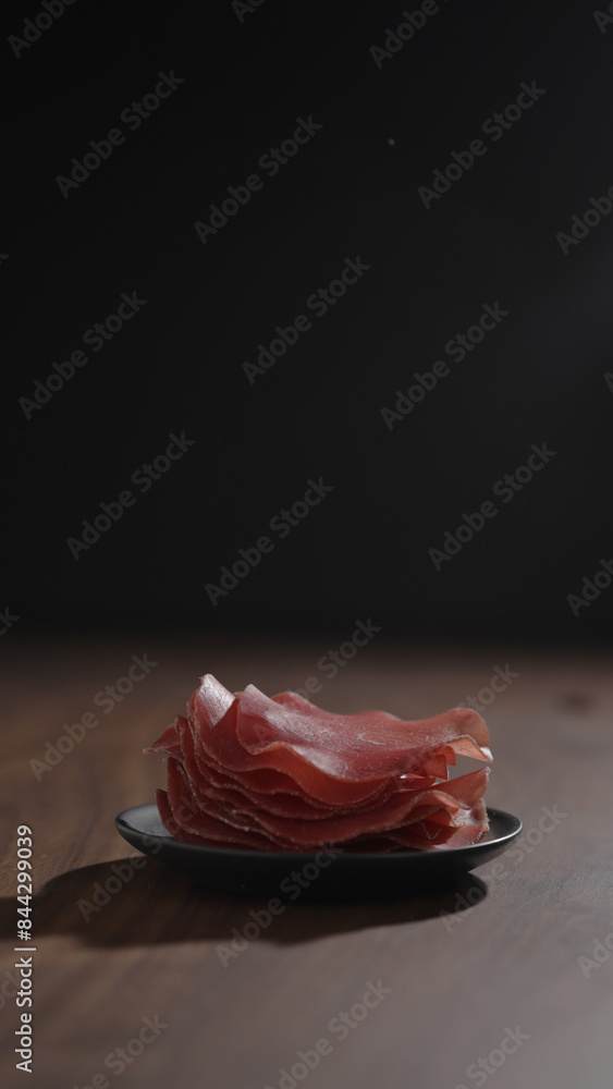 vertical shot bresaola slices on saucer on walnut wood table vertical shot bresaola slices on saucer on walnut wood table