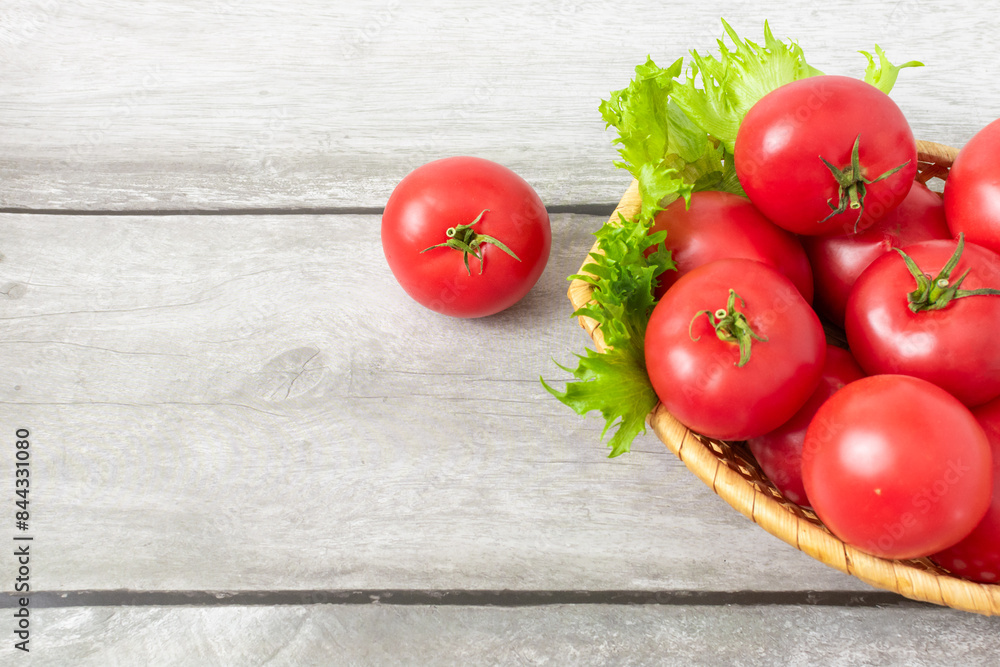 Ripe tomatoes in a basket with lettuce leaves on a light wooden background Ripe tomatoes in a basket with lettuce leaves on a light wooden background