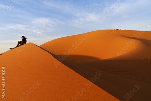 group of tourists sitting on the sand dune of Erg Chebbi with a solitary man in the foreground