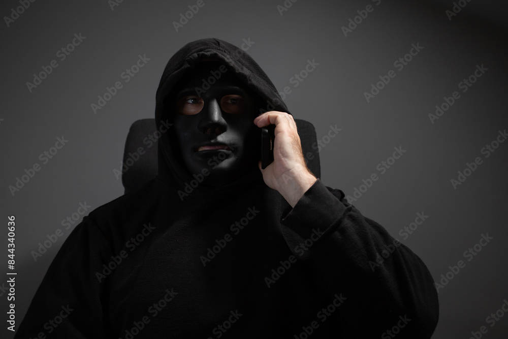 Money swindler, a man in a mask talking on the phone, committing online theft of digital currency. Money swindler, a man in a mask talking on the phone, committing online theft of digital currency.