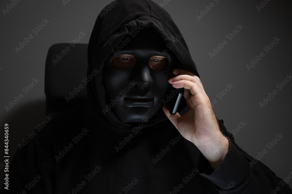 Money swindler, a man in a mask talking on the phone, financial fraud through mobile banking. Money swindler, a man in a mask talking on the phone, financial fraud through mobile banking.