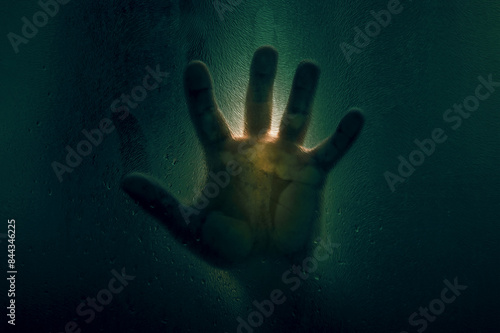 Horror scene of a man against wet glass. Hand against the background of a wet glass bathroom wall. Toned image.