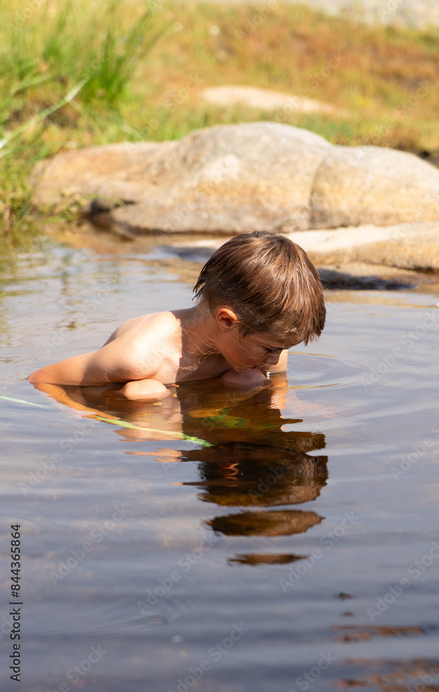 Fototapeta premium Boy bathing in a river looking into something
