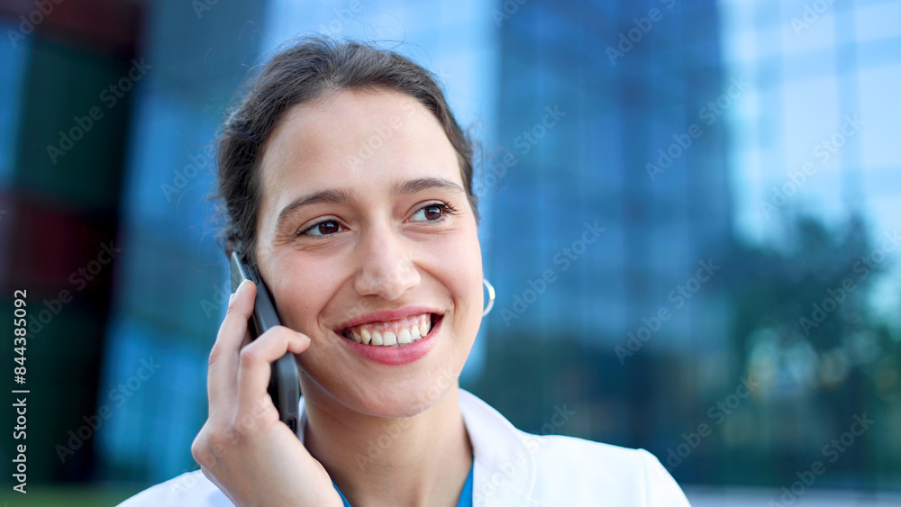 Young female doctor standing in front of her medical clinic and talking on mobile phone Young female doctor standing in front of her medical clinic and talking on mobile phone