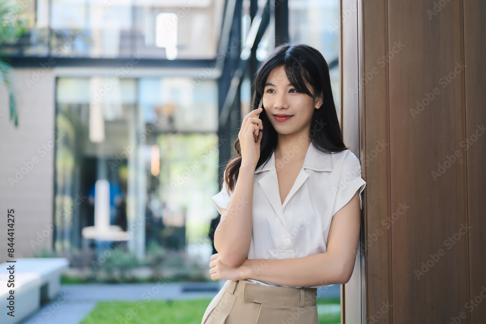 Young Woman Talking on Smartphone Outdoors in Modern Urban Setting, Business Casual Attire, Professional Communication, Confident Expression, Contemporary Architecture Background Young Woman Talking on Smartphone Outdoors in Modern Urban Setting, Business Casual Attire, Professional Communication, Confident Expression, Contemporary Architecture Background