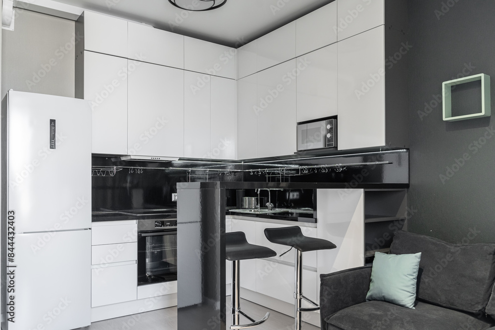 modern minimalistic black and white kitchen. Kitchen with built-in appliances, microwave, oven, refrigerator. The countertop and dining area in the kitchen are made of black stone. Black chairs modern minimalistic black and white kitchen. Kitchen with built-in appliances, microwave, oven, refrigerator. The countertop and dining area in the kitchen are made of black stone. Black chairs