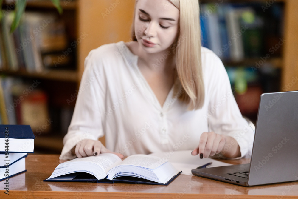 a young woman with blond hair who sits at a table in a library or study hall. concept of learning and self-development. The woman is immersed in the process of reading and analyzing information, which a young woman with blond hair who sits at a table in a library or study hall. concept of learning and self-development. The woman is immersed in the process of reading and analyzing information, which