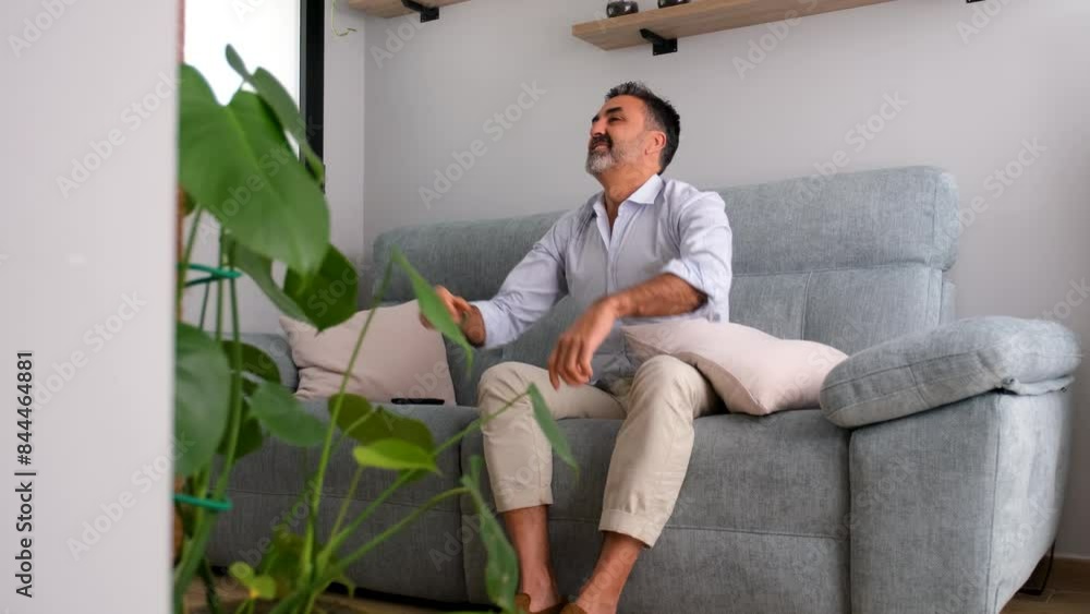 A mature man celebrating a goal of his soccer team sits on a couch. Man watching sports at TV A mature man celebrating a goal of his soccer team sits on a couch. Man watching sports at TV