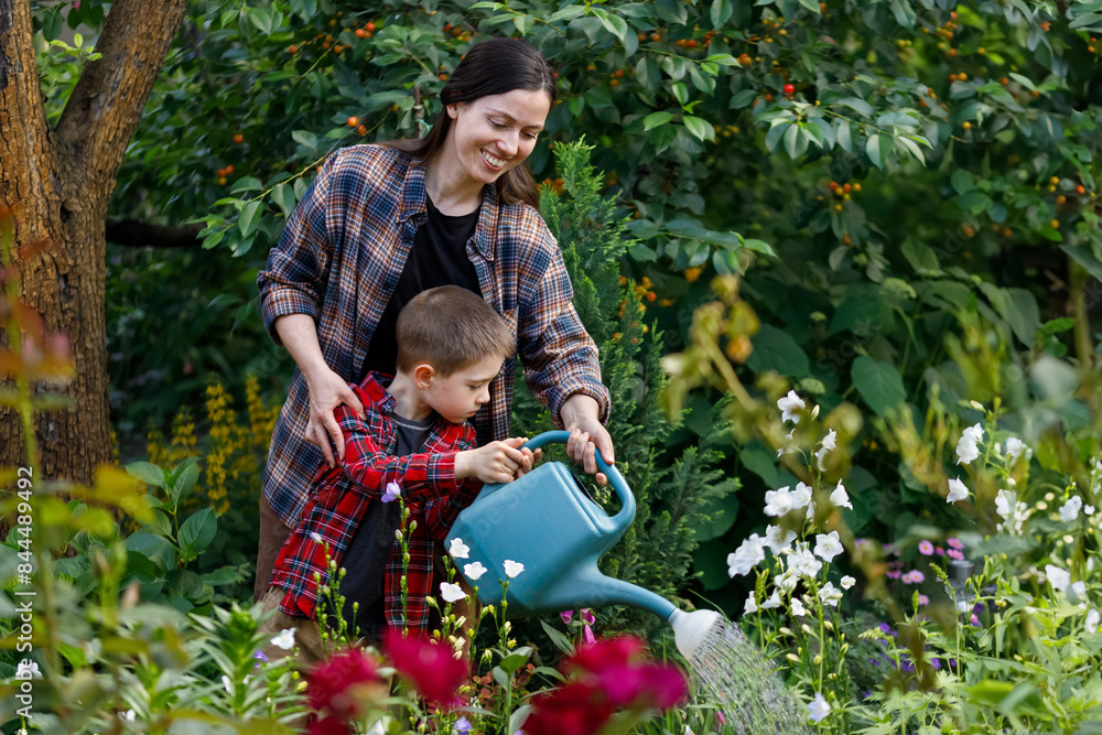 smiling mother gardener with child boy water the flowers from watering can in garden smiling mother gardener with child boy water the flowers from watering can in garden