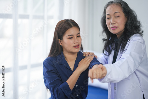 A doctor assists a young woman with a shoulder and arm examination in a medical office. They are discussing possible treatment options.