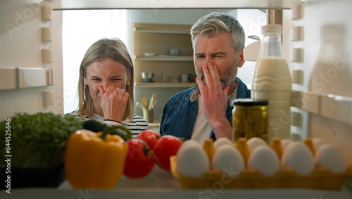 POV Point of view from inside fridge adult couple feeling bad disgusting unpleasant smell from broken refrigerator spoiled rotten food meal middle-aged man and woman awful smelling stink from freezer