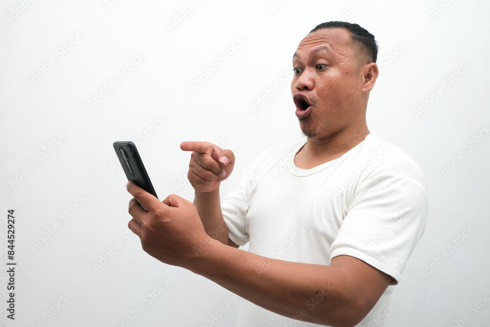 photo of the shocked expression of an Asian man looking at a mobile phone in his hand photo of the shocked expression of an Asian man looking at a mobile phone in his hand