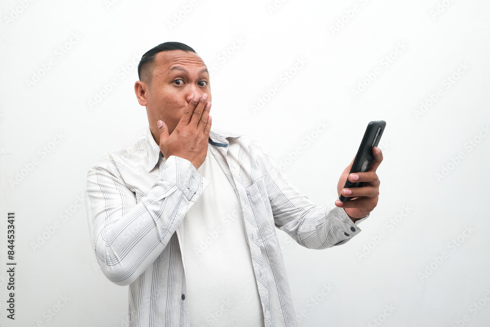 photo of the shocked expression of an Asian man looking at a mobile phone in his hand photo of the shocked expression of an Asian man looking at a mobile phone in his hand