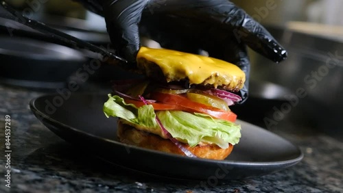 The chef puts a cutlet with cheese in a hamburger in black gloves slow motion