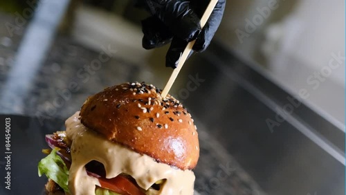 Chef inserting a wooden stick into a hamburger in the kitchen black background slow motion