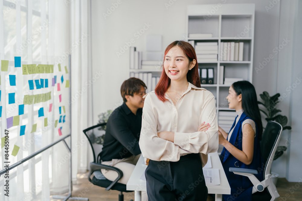 Confident Businesswoman in Modern Office with Colleagues Collaborating in Background, Bright Workspace with Sticky Notes on Glass Wall, Professional Teamwork and Innovation Concept Confident Businesswoman in Modern Office with Colleagues Collaborating in Background, Bright Workspace with Sticky Notes on Glass Wall, Professional Teamwork and Innovation Concept