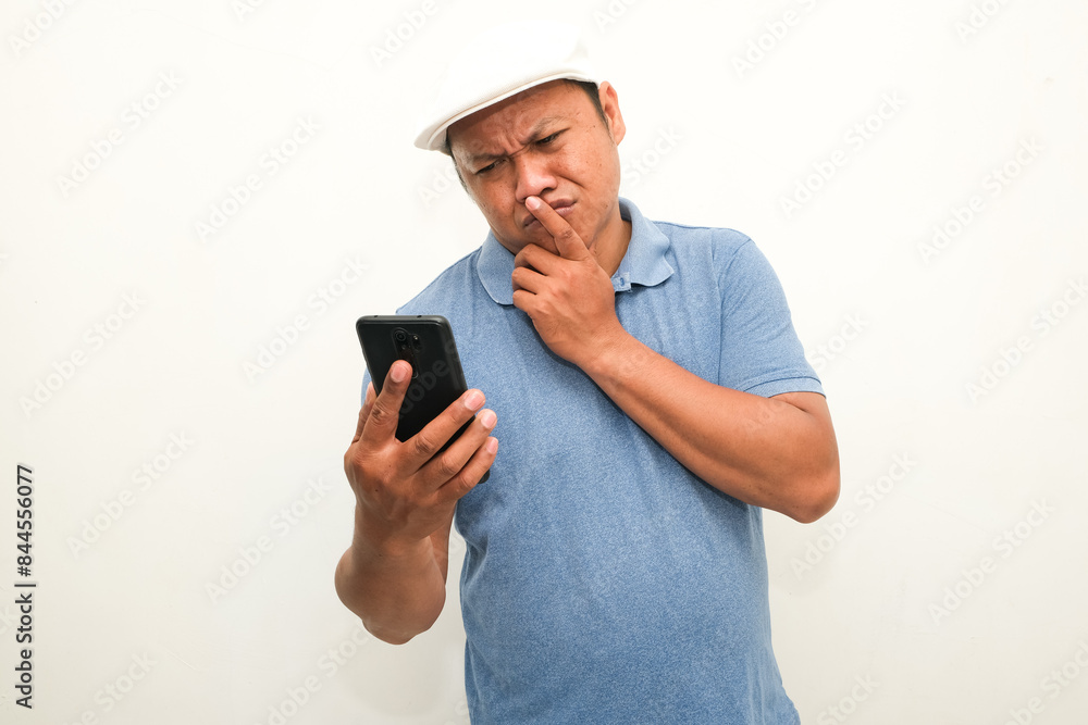 Adult Asian man thinking about something while holding mobile phone Adult Asian man thinking about something while holding mobile phone