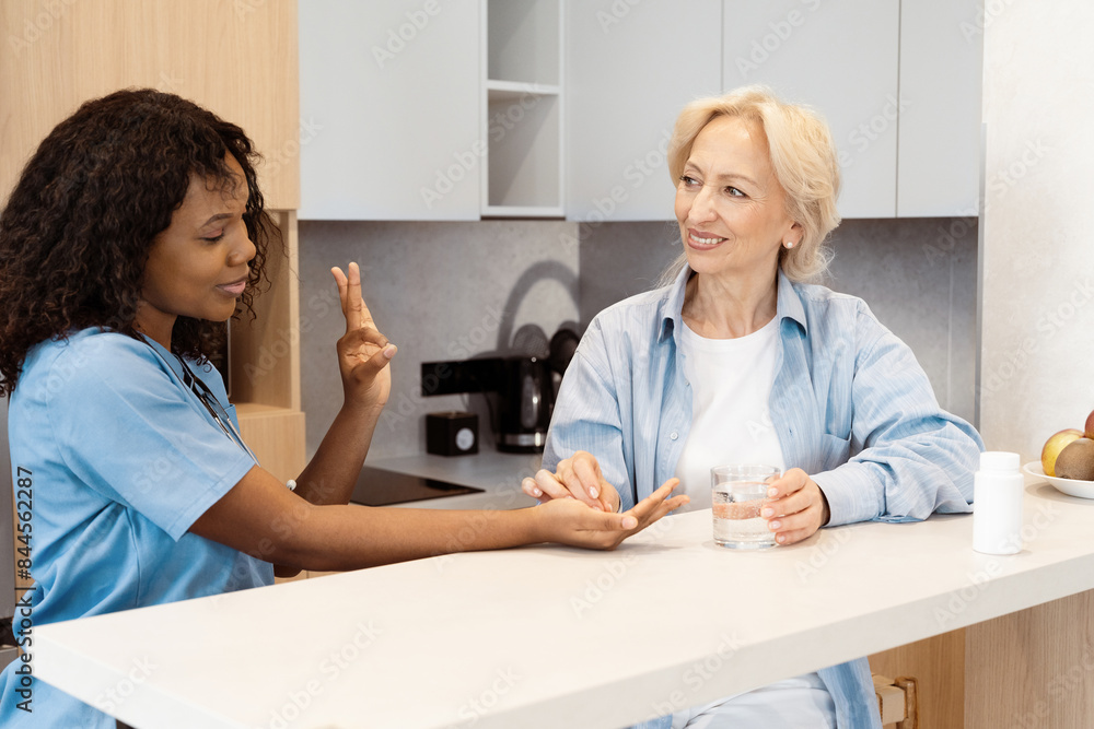 Obraz premium Nurse And Senior Woman Having Friendly Conversation Over Medication In Kitchen