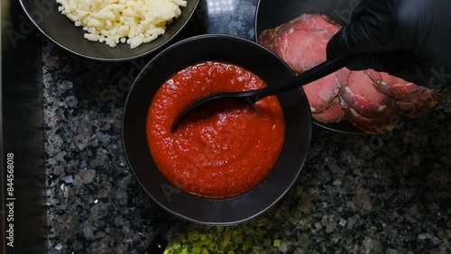 Chef in black gloves puts red sauce with a spoon from a pizza plate slow motion close-up