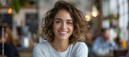 Portrait of a beautiful smiling woman with curly hair sitting at a table in a modern office, wearing casual