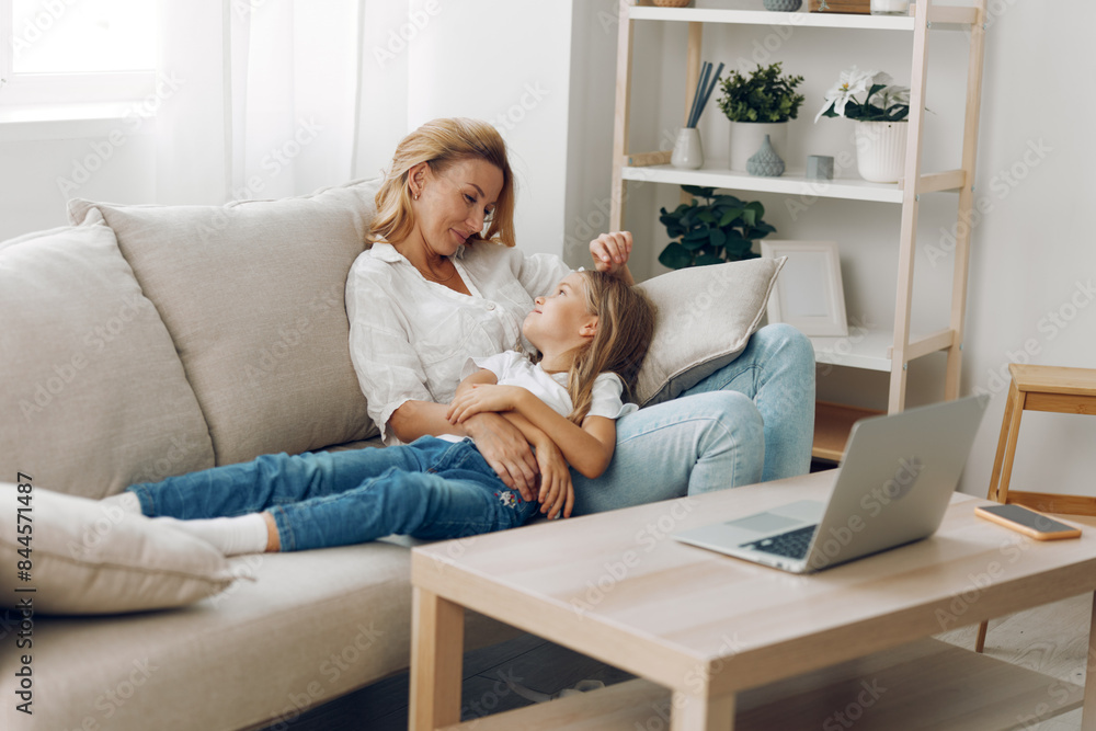 Mother and daughter bonding time smiling while watching educational videos on laptop in cozy living room
