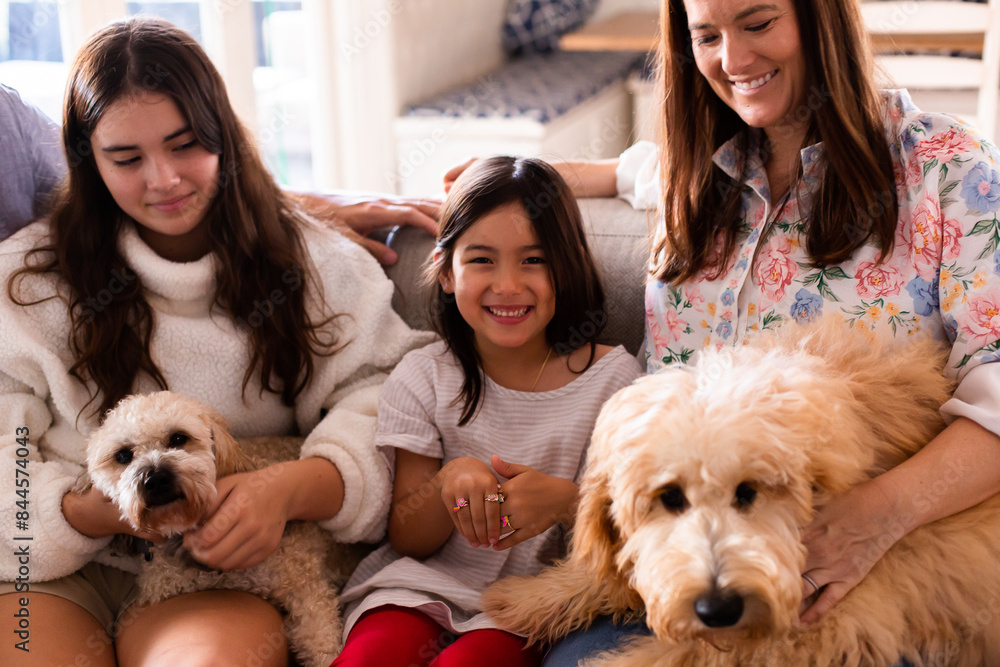 Youngest daughter smiling at the camera sitting next to her mum, big sister and pet dogs on lounge Youngest daughter smiling at the camera sitting next to her mum, big sister and pet dogs on lounge