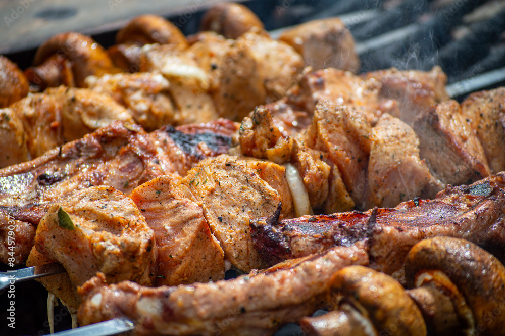 Grilled pieces of pork meat and mushrooms on metal skewers. Shashlik or shish kebab prepared on barbecue grill over hot charcoal with grilled vegetables. Grilled pieces of pork meat and mushrooms on metal skewers. Shashlik or shish kebab prepared on barbecue grill over hot charcoal with grilled vegetables.