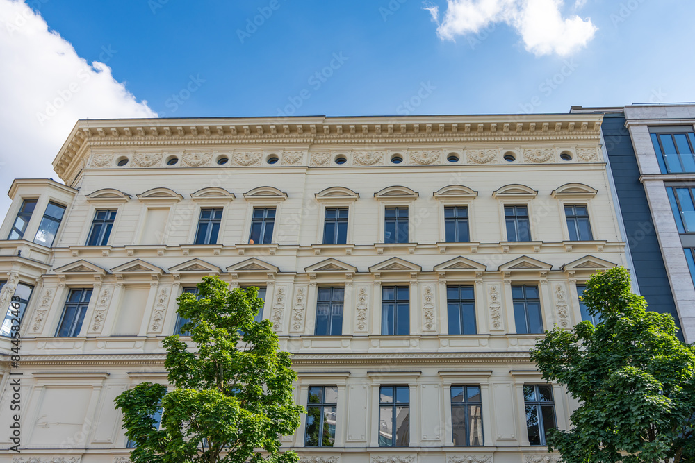Obraz premium A large building with a lot of windows and a green tree in front of it. The building has a lot of detail and looks very old