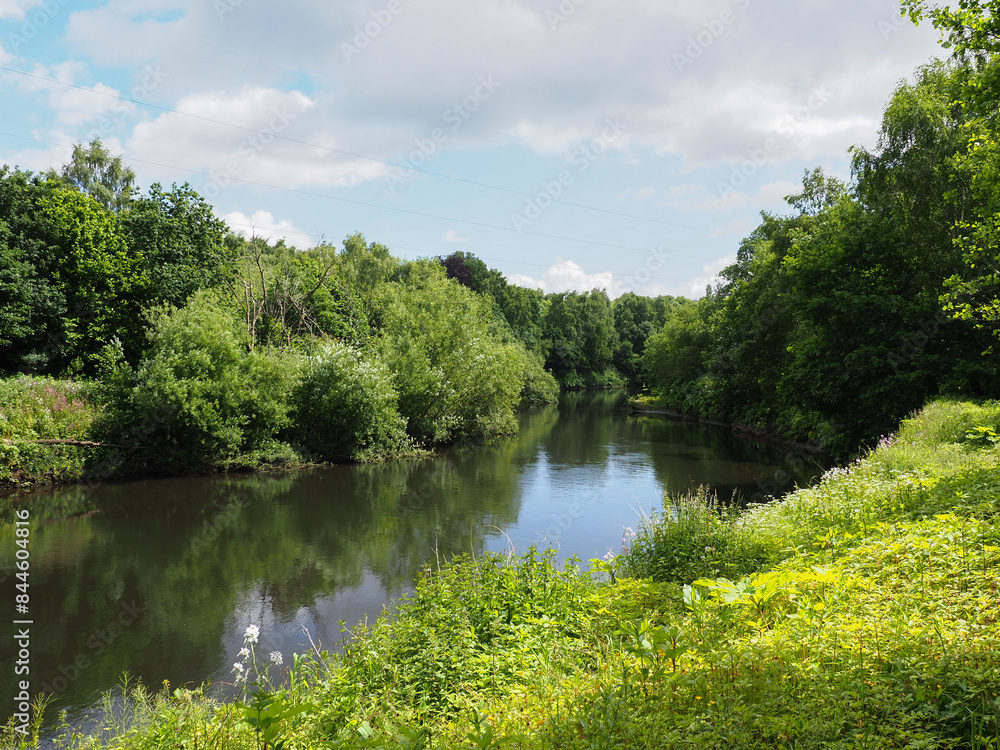 Calm river Irwell flowing through Salford lush green forest with blue skies and fluffy clouds overhead. Calm river Irwell flowing through Salford lush green forest with blue skies and fluffy clouds overhead.