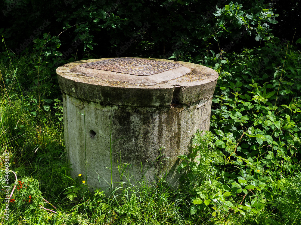 Old concrete well cover in lush forest, showing nature reclaiming man-made structures Old concrete well cover in lush forest, showing nature reclaiming man-made structures