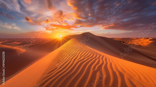 Sunset over desert dunes casts intricate shadows  the sky is ablaze with warm colors  creating serenity.