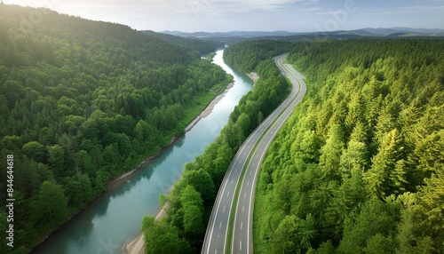 Aerial view, bird's-eye view of a scenic highway following a blue river through a lush green forest.