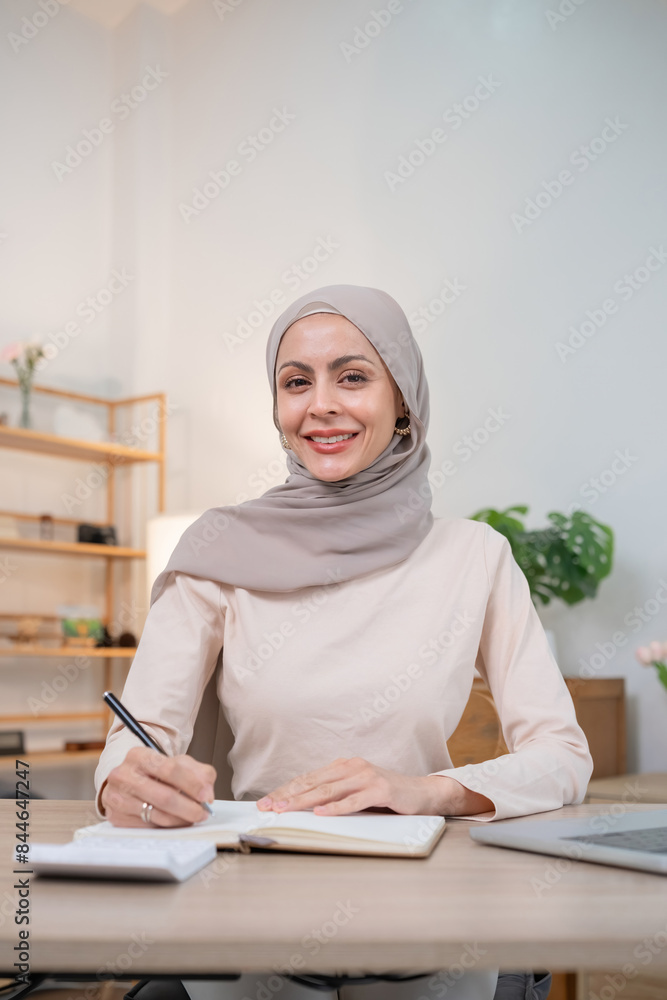 Confident Muslim Woman in Hijab Working at Desk, Smiling and Writing in Notebook, Modern Office Environment, Professional and Empowered, Diverse Workplace, Business and Education Concept Confident Muslim Woman in Hijab Working at Desk, Smiling and Writing in Notebook, Modern Office Environment, Professional and Empowered, Diverse Workplace, Business and Education Concept