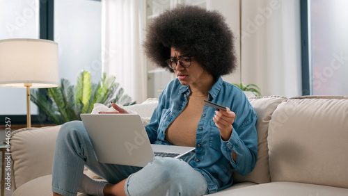 Confused puzzled irritated upset girl buyer African American woman try pay online with laptop credit card failure error mistake secure number shopping problem unsuccessful payment bank trouble at home photo