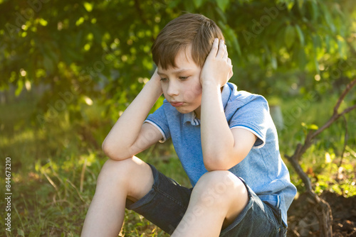 Child boy lonely and sad or bored in nature, disappointed or sitting on grass in backyard lawn alone. Kid, upset and unhappy with melancholy, depressed face or solitude for summer in garden or park