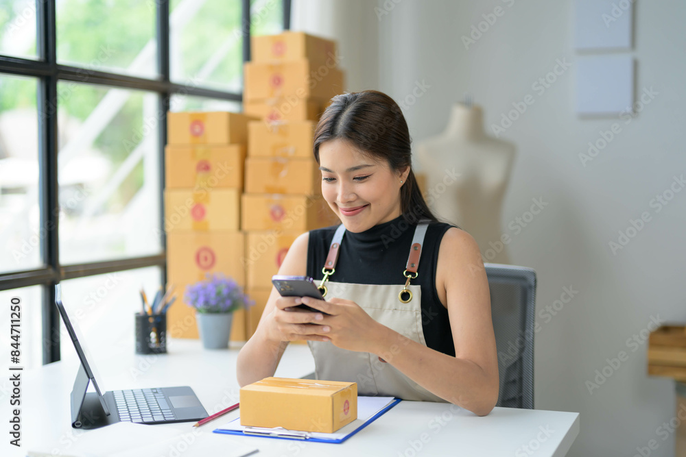 Young Woman Entrepreneur Using Smartphone in Modern Office Surrounded by Shipping Boxes, Small Business Owner Managing Online Orders, E-commerce Startup Concept Young Woman Entrepreneur Using Smartphone in Modern Office Surrounded by Shipping Boxes, Small Business Owner Managing Online Orders, E-commerce Startup Concept