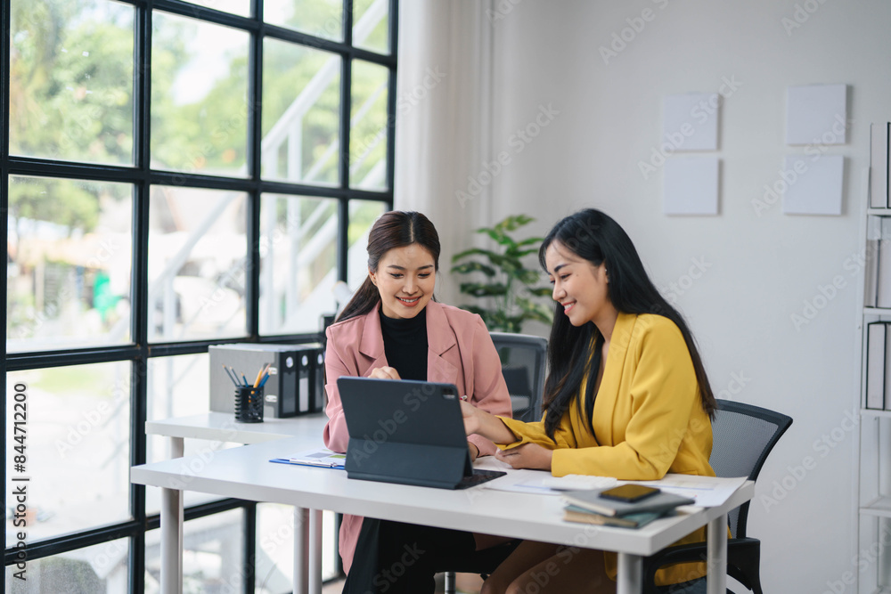 Two Professional Women Collaborating in a Modern Office Setting with Large Windows and Natural Light Two Professional Women Collaborating in a Modern Office Setting with Large Windows and Natural Light