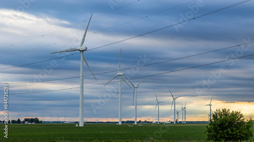 Wind turbines on flat farmland with powerlines and dark, threatening clouds.