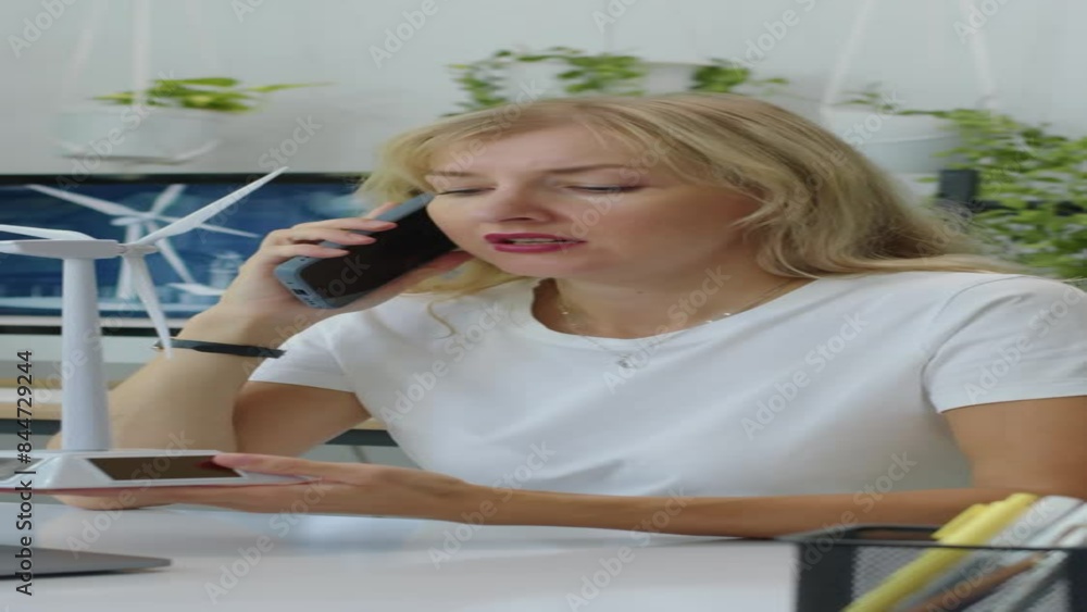 Vertical shot of project manager calling on smartphone when holding wind turbine model at desk in green office Vertical shot of project manager calling on smartphone when holding wind turbine model at desk in green office
