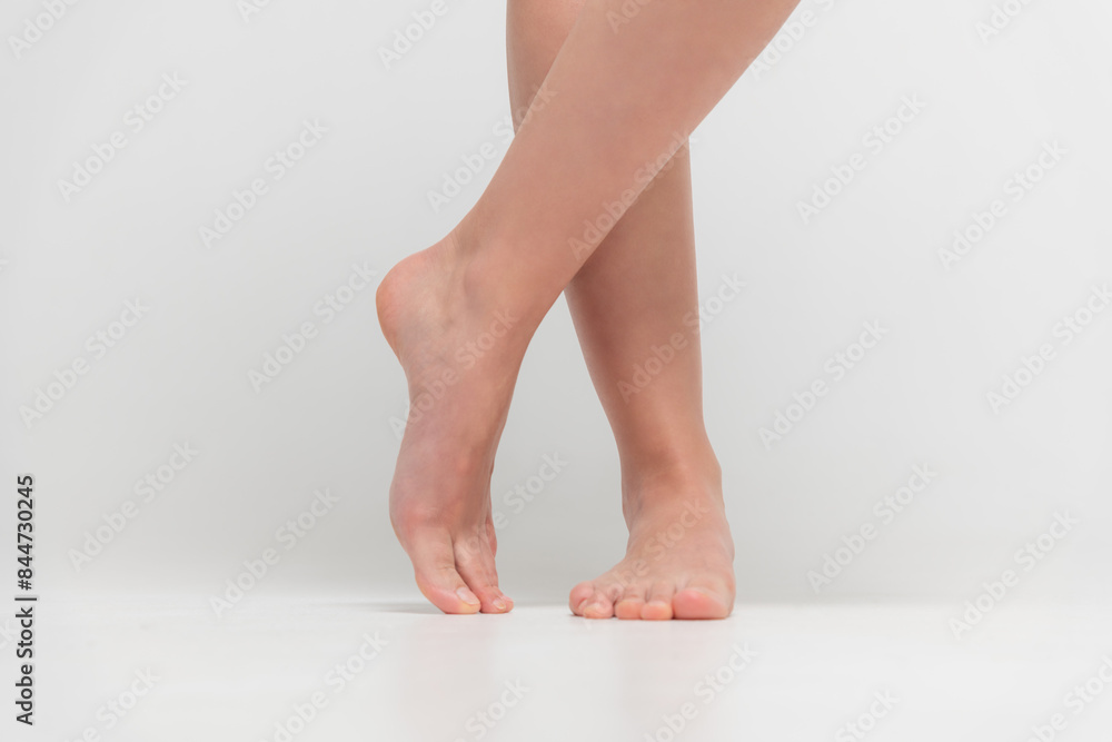 Close-up front view of barefoot woman standing on white floor and showing her feet against gray background. Soft focus. Human body parts. Beauty and skin care theme. Close-up front view of barefoot woman standing on white floor and showing her feet against gray background. Soft focus. Human body parts. Beauty and skin care theme.