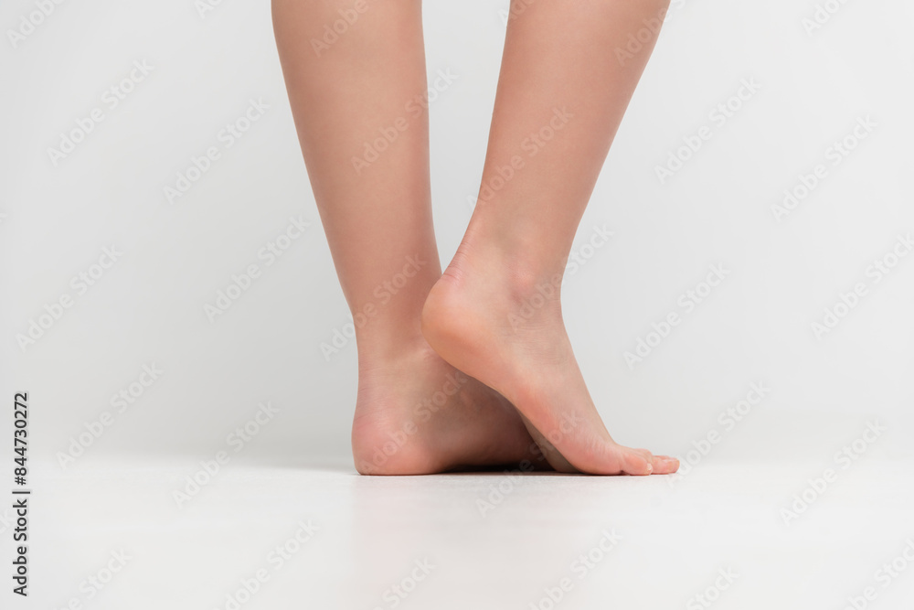 Close-up rear view of barefoot woman standing on white floor and showing her heels against gray background. Soft focus. Human body parts. Beauty and skin care theme. Close-up rear view of barefoot woman standing on white floor and showing her heels against gray background. Soft focus. Human body parts. Beauty and skin care theme.