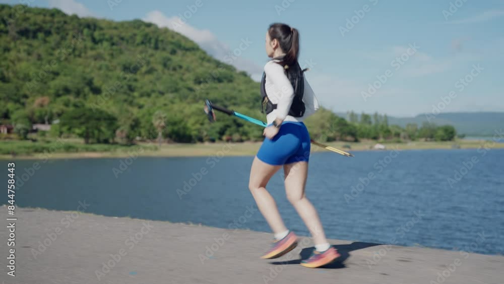 A woman runs on a path near a body of water. She is wearing blue shorts and a white shirt A woman runs on a path near a body of water. She is wearing blue shorts and a white shirt