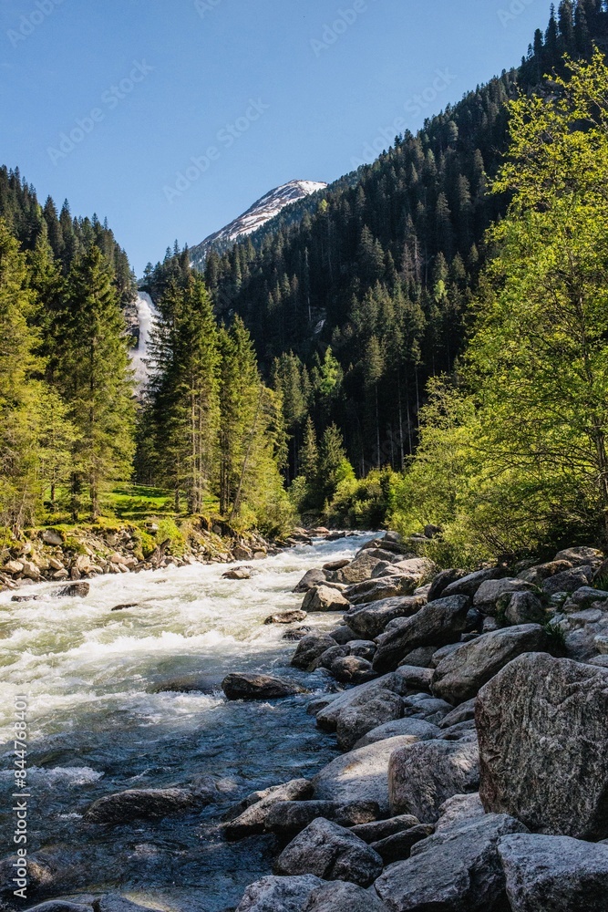 Ein fließender Gebirgsbach in einer waldreichen Berglandschaft mit klarblauem Himmel. Ein fließender Gebirgsbach in einer waldreichen Berglandschaft mit klarblauem Himmel.