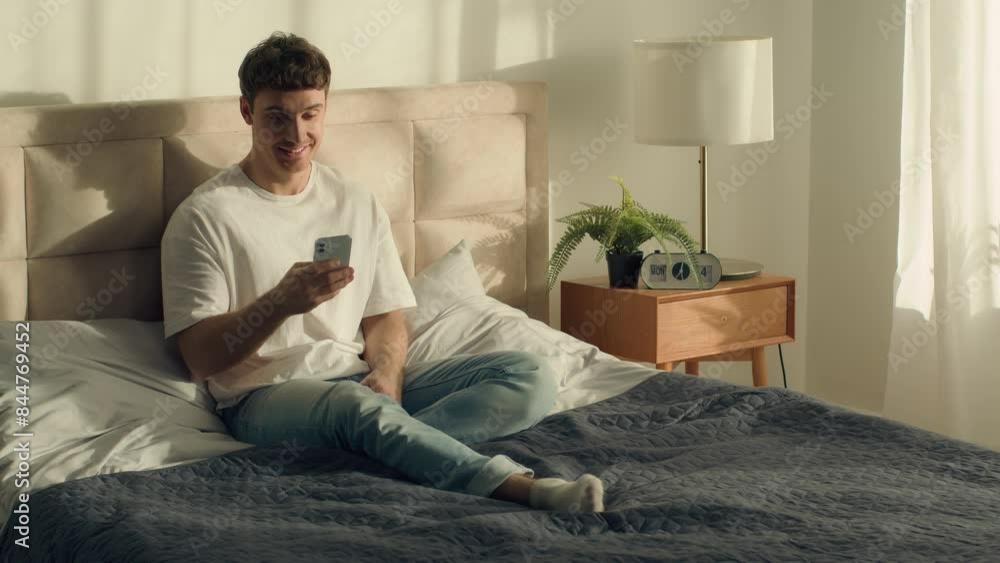 Caucasian European happy man sitting on bed holding using mobile phone smartphone cellphone technology texting online chat internet sms messages smiling home comfort inside male leisure weekend gen z Caucasian European happy man sitting on bed holding using mobile phone smartphone cellphone technology texting online chat internet sms messages smiling home comfort inside male leisure weekend gen z