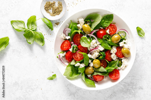 Fresh healthy vegetable Mediterranean salad of feta cheese, tomato, olives, green pepper and green basil leaves, top view