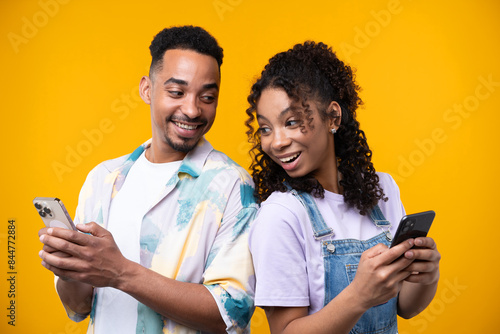 Two hipster friends smiling cheerfully while standing against a yellow background.